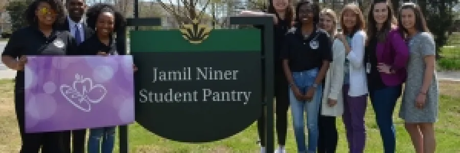 Group of individuals standing around the Jamil Niner Student Pantry. The group on the left is holding a giant Harris Teeter gift card.