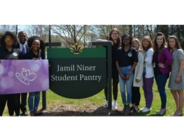 Group of individuals standing around the Jamil Niner Student Pantry. The group on the left is holding a giant Harris Teeter gift card.