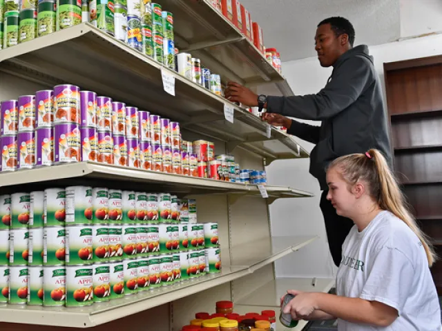 Individuals restocking canned goods on shelves in the Jamil Niner Student Pantry.